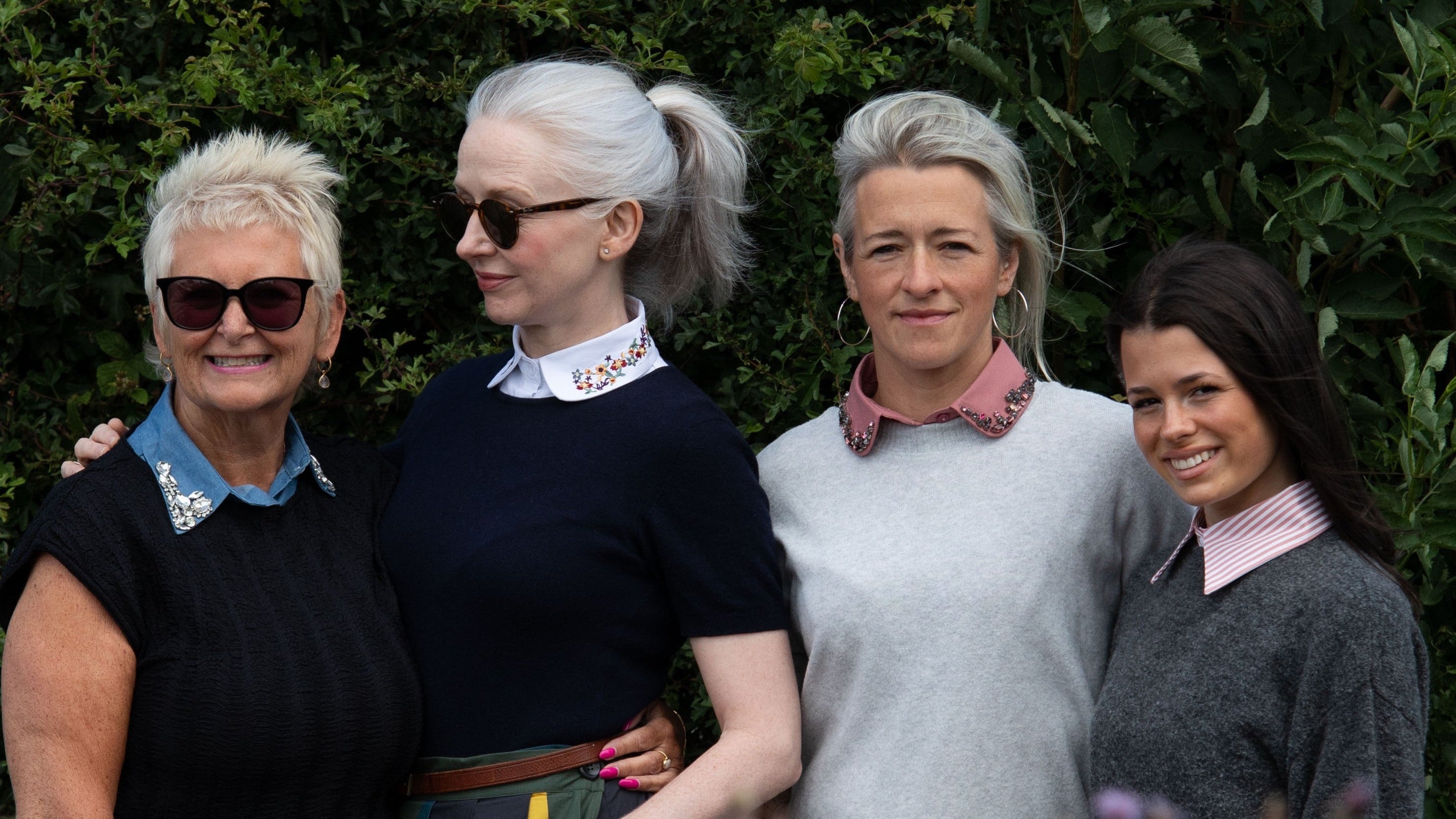 Four women standing together in front of a green hedge